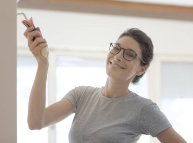 Yeni evinde duvarları boyayan gülümseyen genç kadın: ev dekorasyonu ve DIY konsepti