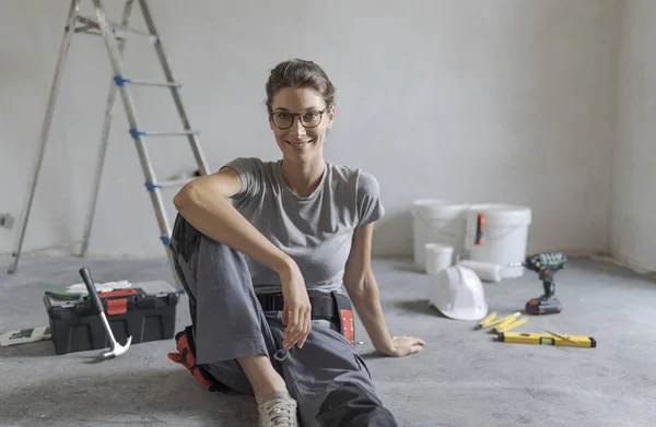 Attractive smiling woman renovating her house, she is sitting on the floor with tools and posing, home makeover concept