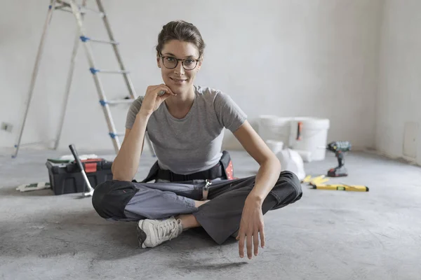 Attractive smiling woman renovating her house, she is sitting on the floor with tools and posing, home makeover concept
