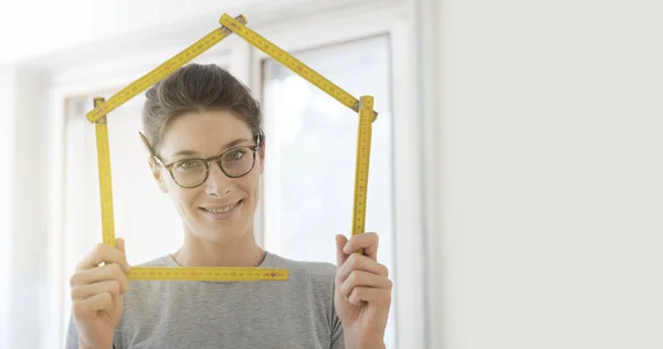 Woman making a house shape with a folding ruler and smiling, home renovation and construction concept