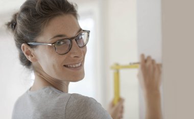 Gülümseyen genç kadın bir ev makyaj yapıyor, o katlanan bir cetvel, DIY ve ev yenileme kavram kullanarak bir duvar ölçmek