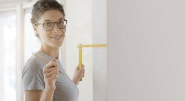Gülümseyen genç kadın bir ev makyaj yapıyor, o katlanan bir cetvel, DIY ve ev yenileme kavram kullanarak bir duvar ölçmek
