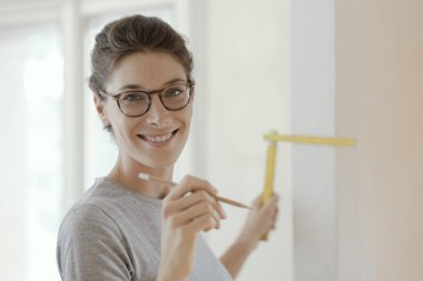 Gülümseyen genç kadın bir ev makyaj yapıyor, o katlanan bir cetvel, DIY ve ev yenileme kavram kullanarak bir duvar ölçmek