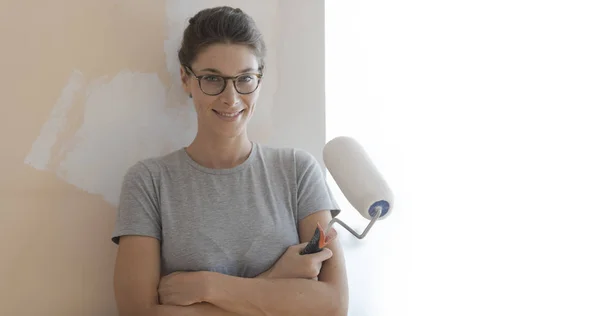 Smiling young woman painting walls in her new house: home renovation and DIY concept