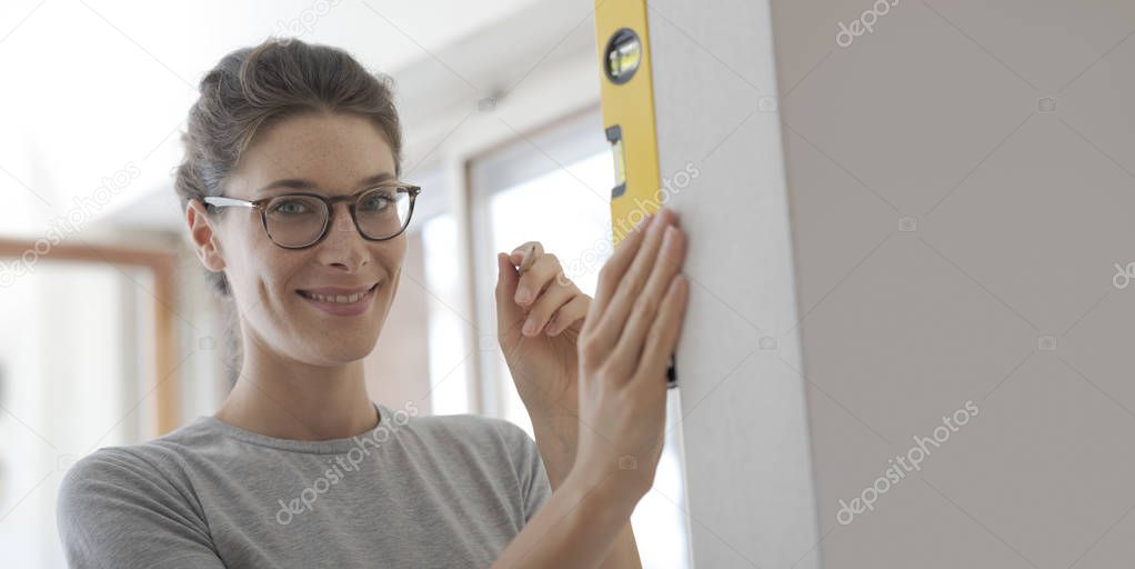 Young woman working with a spirit level and checking the surface of a wall, home renovation and construction concept