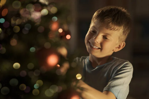 赤いつまらないものでクリスマス ツリーを飾ってる陽気な男の子 休日と小児コンセプト — ストック写真