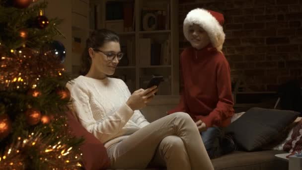 一个戴着圣诞老人帽子的开朗男孩分散了他母亲的注意力 她在给他发痒 度假和生活方式的概念 — 图库视频影像