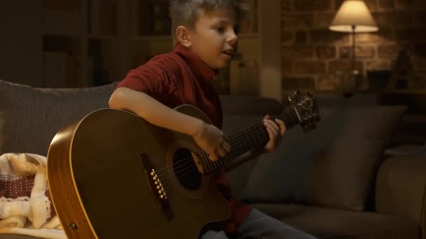 Cute Young Boy Sitting Sofa Home Playing His Guitar Music — Stock Video