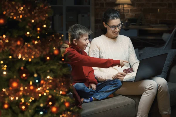 幸せな母と息子のクリスマス プレゼント家庭でクレジット カードでのオンライン ショッピングを行う ラップトップ フォア グラウンドでクリスマス ツリーに接続しています — ストック写真