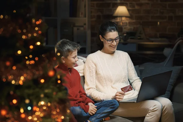 幸せな母と息子のクリスマス プレゼント家庭でクレジット カードでのオンライン ショッピングを行う ラップトップ フォア グラウンドでクリスマス ツリーに接続しています — ストック写真