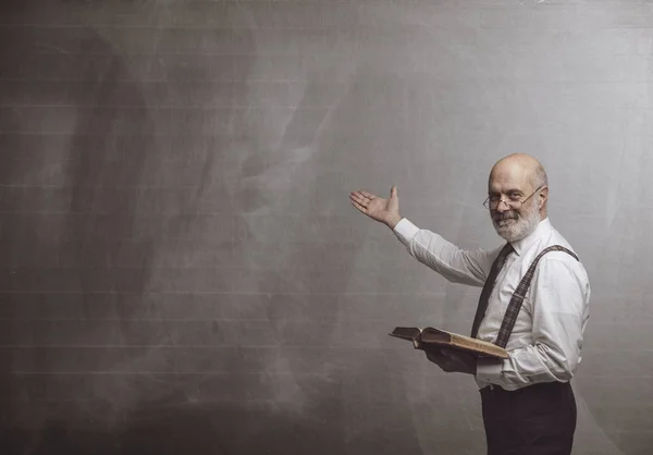 Smiling confident professor teaching and pointing at the blackboard: academic education and learning concept