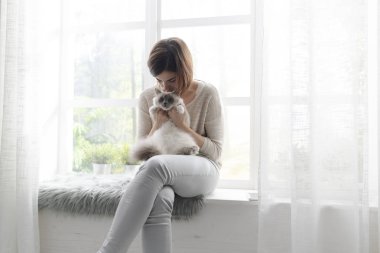 Pencere kenarında oturan ve onun güzel birman kedisi, Evcil hayvan ve yaşam tarzı kavramı sarılma kadın