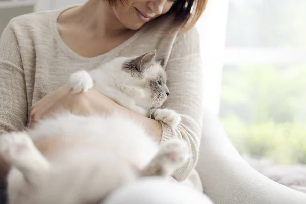 若い幸せな女リビング ルームの肘掛け椅子に座って 彼女の美しい猫をかわいがる — ストック写真
