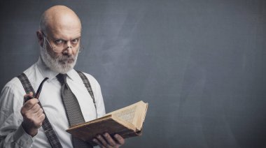 Confident senior professor smoking a pipe and reading an old book, knowledge and education concept clipart