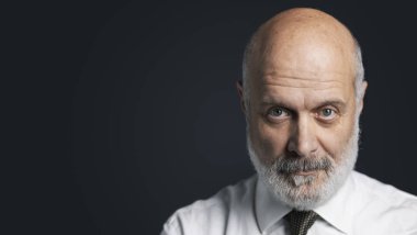 Orta koyu arka plan üzerinde poz ve kameraya bakarak yaş işadamı emin