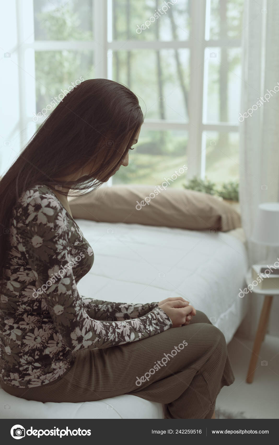 Uma mulher triste, sentada na beirada da cama, de noite. Conceito
