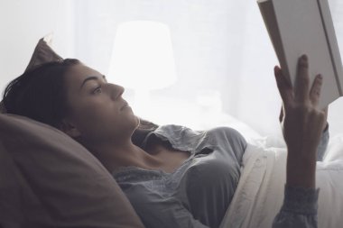 Genç güzel kadın yatakta yatan ve gece geç saatlerde bir kitap okuma