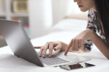 Evde yatakta yatıyordu ve onun laptop, yaşam tarzı ve teknoloji kavramı ile çalışan genç kadın