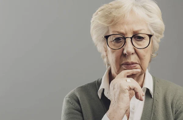 Nachdenkliche Seniorin denkt mit der Hand am Kinn — Stockfoto