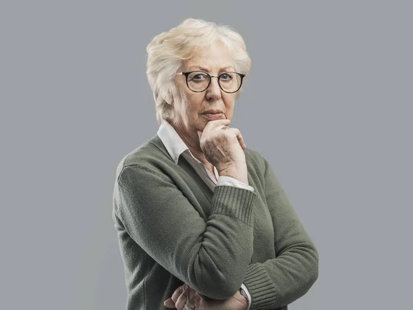 Nachdenkliche Seniorin denkt mit der Hand am Kinn — Stockfoto