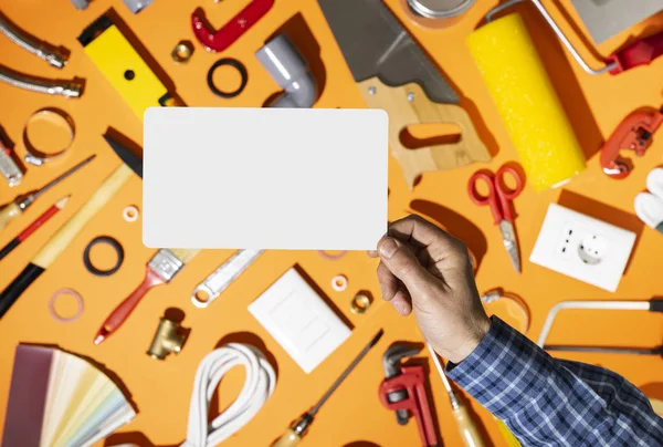 Professional repairman holding a blank card and hardware tools — Stock Photo, Image