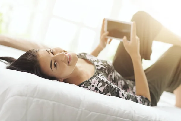 Mujer joven feliz relajarse en la cama y conectarse en línea —  Fotos de Stock