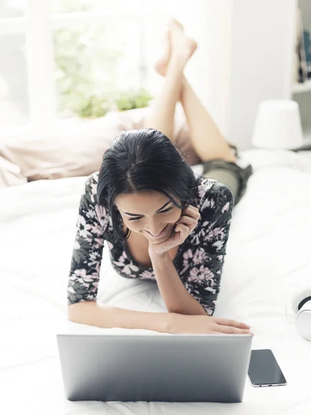 Frau liegt auf Bett und verbindet sich mit ihrem Laptop — Stockfoto