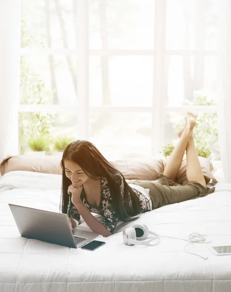 Frau liegt auf Bett und verbindet sich mit ihrem Laptop — Stockfoto