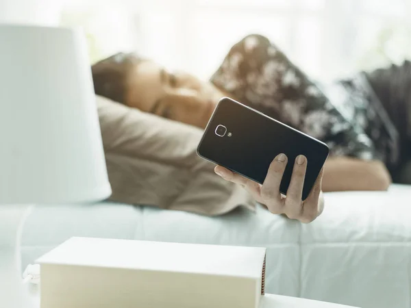 Jovem deitada na cama e conectando-se com seu telefone — Fotografia de Stock