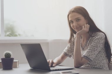 Evde dizüstü bilgisayarıyla çalışan genç bir kadın.