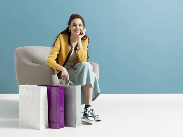 Glückliche Frau sitzt nach dem Einkaufen auf einem Sessel — Stockfoto