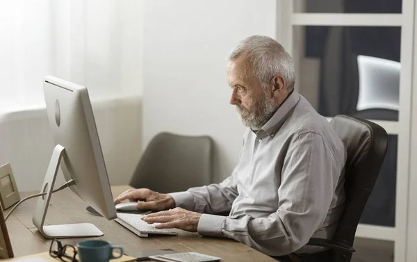 Uomo anziano che usa il suo computer a casa — Foto Stock