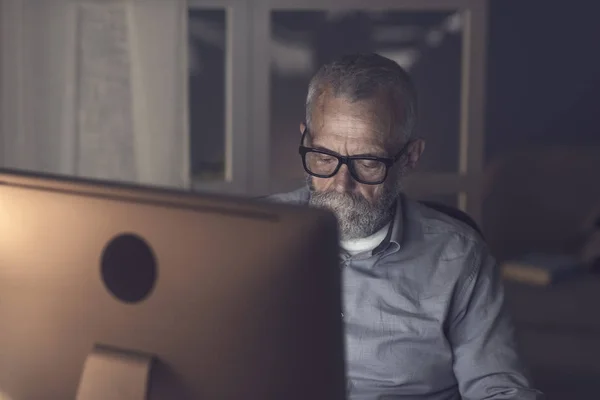 Homem sênior trabalhando com seu computador à noite — Fotografia de Stock