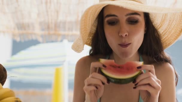 Gelukkige jonge vrouw die watermeloen op het strand eet — Stockvideo
