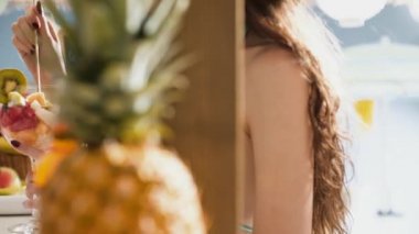 Sahilde meyve salatası yiyen gülümseyen genç kadın