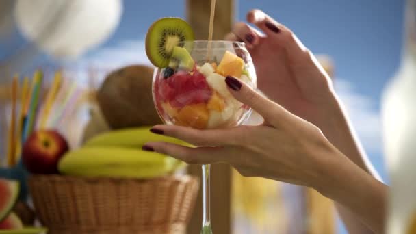 Lächelnde junge Frau isst Obstsalat am Strand — Stockvideo