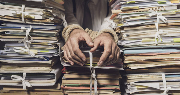 Деловые руки связаны верёвкой и куча бумажной работы.
