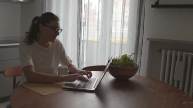 Mutfakta oturup laptopuyla sohbet eden mutlu bir kadın.