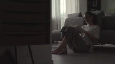 Kadın evde dinleniyor ve kitap okuyor.