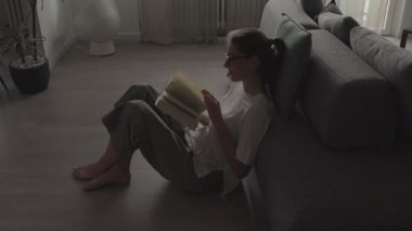 Kadın evde dinleniyor ve kitap okuyor.