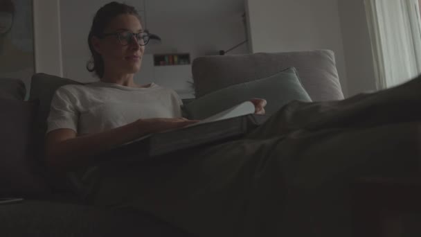 Mulher relaxante em casa e olhando para fotos antigas em um álbum de fotos — Vídeo de Stock