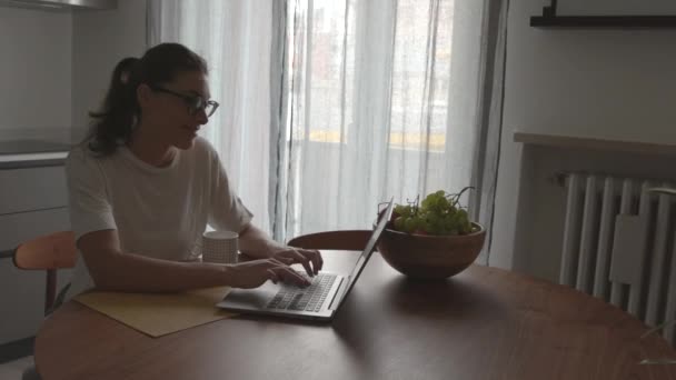 Mujer feliz sentada en la cocina y charlando con su portátil — Vídeos de Stock