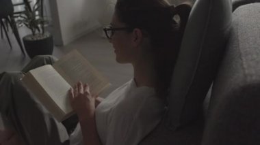 Kadın evde dinleniyor ve kitap okuyor.