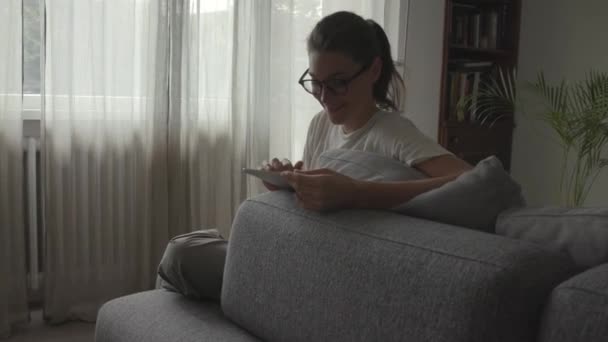 Жінка розслабляється у вітальні і спілкується зі своїм планшетом — стокове відео