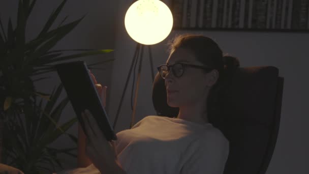 Kobieta spoczywająca na fotelu i łącząca się z tabletem — Wideo stockowe