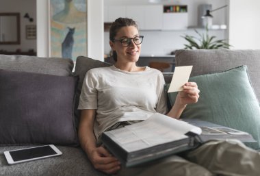 Kanepede dinlenen ve fotobook 'taki eski resimlere bakan kadın.