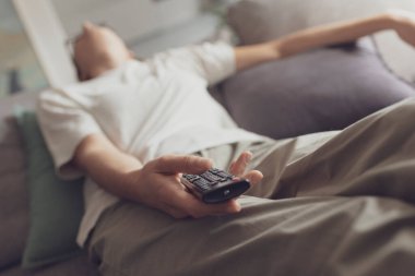 Sıkıcı kadın TV izlerken kanepede uyuyakalıyor, uzaktan kumandayı elinde tutuyor.