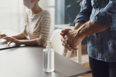 Ofiste birlikte çalışan iş adamları ve işyerindeki güvenlik önlemleri: bir erkek ellerine dezenfektan sürüyor
