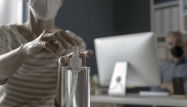 Coronavirüs salgını sırasında iş yerinde çalışan bir kadın maske takıyor ve ellerine dezenfektan sürüyor.