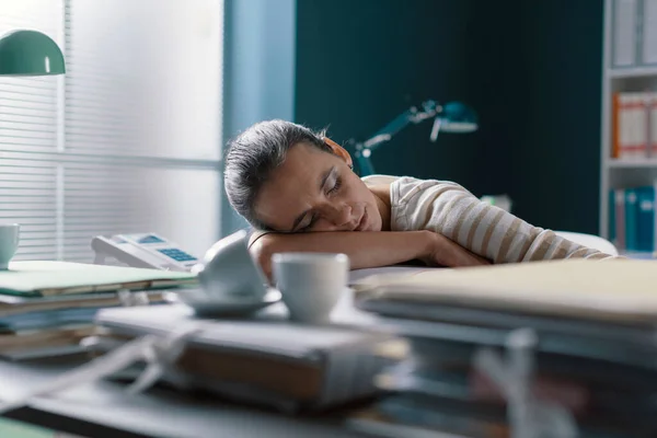 精疲力竭的女商人睡在桌子上 疲惫不堪 靠在一堆文书工作上 — 图库照片
